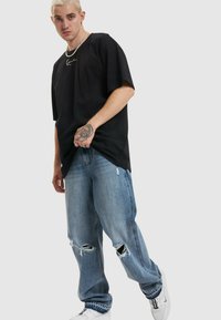 Svart oversized T-skjorte med logo på brystet, kombinert med lyseblå slitt baggy jeans og hvite joggesko, med rett passform og frynset nederkant.