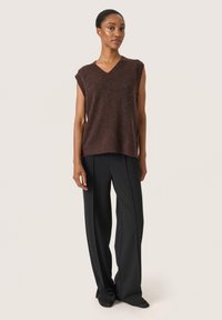 Top tricot bej, fără mâneci, cu decolteu în V și textură moale, asortat cu pantaloni negri, cu talie înaltă și croială largă. Design minimalist.