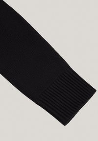 Czarna dzianinowa rękawica z prążkowanym mankietem, o gładkiej teksturze i jednolitym wzorze stawów, widok z boku na jasnym tle.