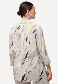 Camicia in tessuto leggero con un design fluido; presenta motivi astratti gialli, grigi e neri, con maniche lunghe e polsini abbottonati.