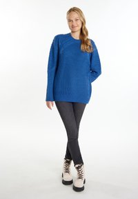 Maglione azzurro lavorato a maglia con un motivo a trame e maniche lunghe, abbinato a jeans grigi scuri e stivaletti beige con lacci.