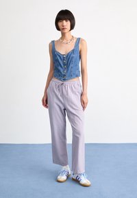 Denim crop top med knäppning, ljuslila vida byxor och vita sneakers med blå och lila ränder. Släta texturer och avslappnad passform.