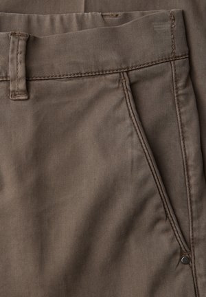 Primo piano di pantaloni marroni di cotone che mostrano la tasca anteriore, l'asola per la cintura e i dettagli delle cuciture.