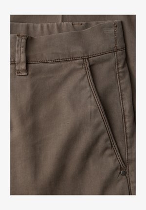 Gros plan sur un pantalon en coton marron montrant la poche avant, la boucle de ceinture et les détails de couture.