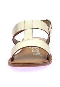 Sandal in oro metallico con cinturini, suola piatta, fibbia regolabile e finitura in pelle liscia. Soletta beige chiaro con logo impresso.