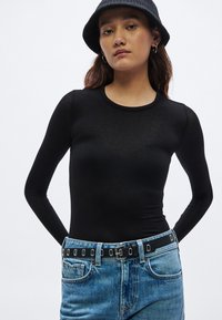 Zwart nauwsluitend longsleeve top met een ronde hals, gecombineerd met lichtgewassen spijkerbroek en een zwarte gespikte riem.