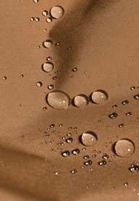 Vanddråber på et struktureret, brunt nylonstof, der viser en glat overflade med en let glans og varierende størrelser af vandperler.