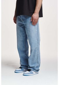 Ljusblå jeans i denim, lös passform, med raka ben och subtil blekning. Matchas med vita och blå låga sneakers med svarta skosnören.