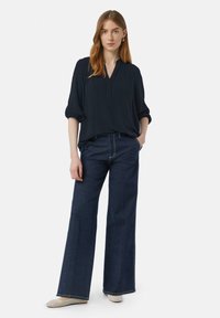 Granatowa bluzka z dekoltem w serek i rękawami 3/4, w połączeniu z ciemnoniebieskimi jeansami z wysokim stanem i szerokimi nogawkami oraz plecionymi płaskimi butami.