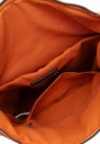 Interno in tessuto arancione di una borsa, con due scomparti e una tasca con zip, texture liscia e hardware della zip nera.