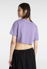 Kaos lavender crop dalam kain lembut dengan lengan pendek dan leher bulat. Dipadukan dengan rok hitam berpinggang elastis, memperlihatkan perut.