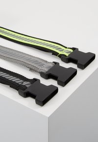 Trīs siksnas ar melniem plastmasas sprādzēm: viena melna ar pelēku svītru, viena pelēka un viena melna ar zaļu svītru. Tekstūrēts audums.