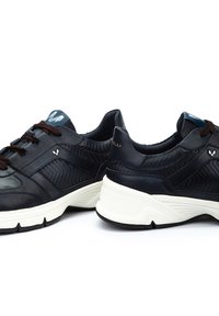 Musta nahkakengät, joissa on verkko-osia, ruskeat nauhat, valkoinen väliosa ja sininen logoaalto. Varustettu pehmustetulla kantapäällä ja teksturoiduilla paneeleilla.