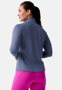 Maglia atletica a maniche lunghe in morbido tessuto blu chiaro con colletto alto, abbinata a leggings rosa vivace. Presenta cuciture piatte e un design aderente.