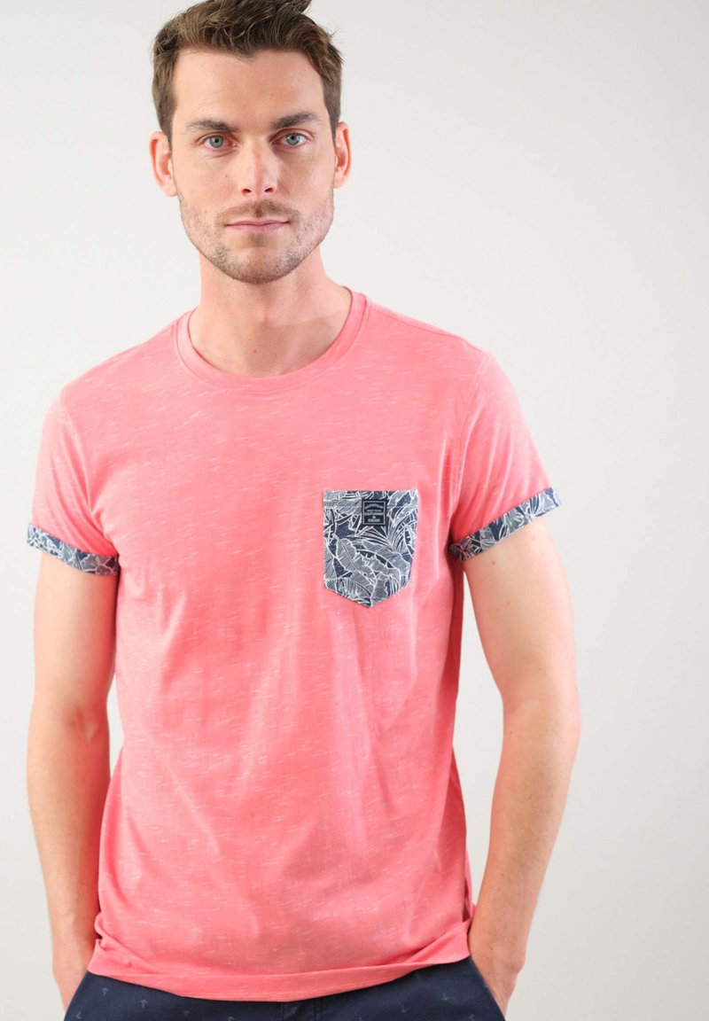 Camisa de manga corta color rosa con un acabado texturizado, que presenta un bolsillo en contraste con un patrón floral azul y mangas enrolladas.