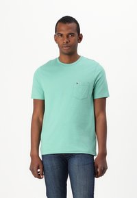 Mint green cotton t-shirt with a crew neck, short sleeves, and a left chest pocket featuring a small logo detail. Worn with blue jeans.