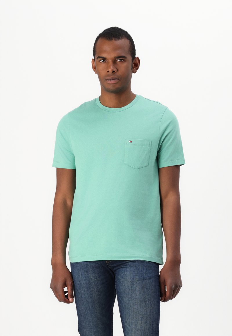 Mint green cotton t-shirt with a crew neck, short sleeves, and a left chest pocket featuring a small logo detail. Worn with blue jeans.