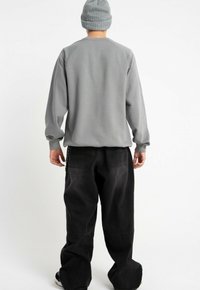 Szary sweatshirt z długimi rękawami, ściągaczem przy szyi i luźnym krojem, zestawiony z czarnymi spodniami o szerokich nogawkach z bocznymi kieszeniami i subtelnymi przeszyciami.