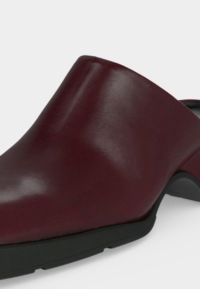 Σκούρο μπορντό δερμάτινο παπούτσι mule με στρογγυλεμένο μύτη και χαμηλό μαύρο τακούνι σε ανοιχτό φόντο.