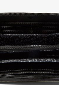Portafoglio nero con chiusura a zip, multiple fessure per carte e rivestimento interno con motivo a fiori bianchi e grigi. Finitura testurizzata.