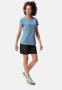 Camiseta atlética de manga corta azul claro con cuello redondo, combinada con pantalones cortos negros y zapatillas de correr verdes con suelas naranjas.