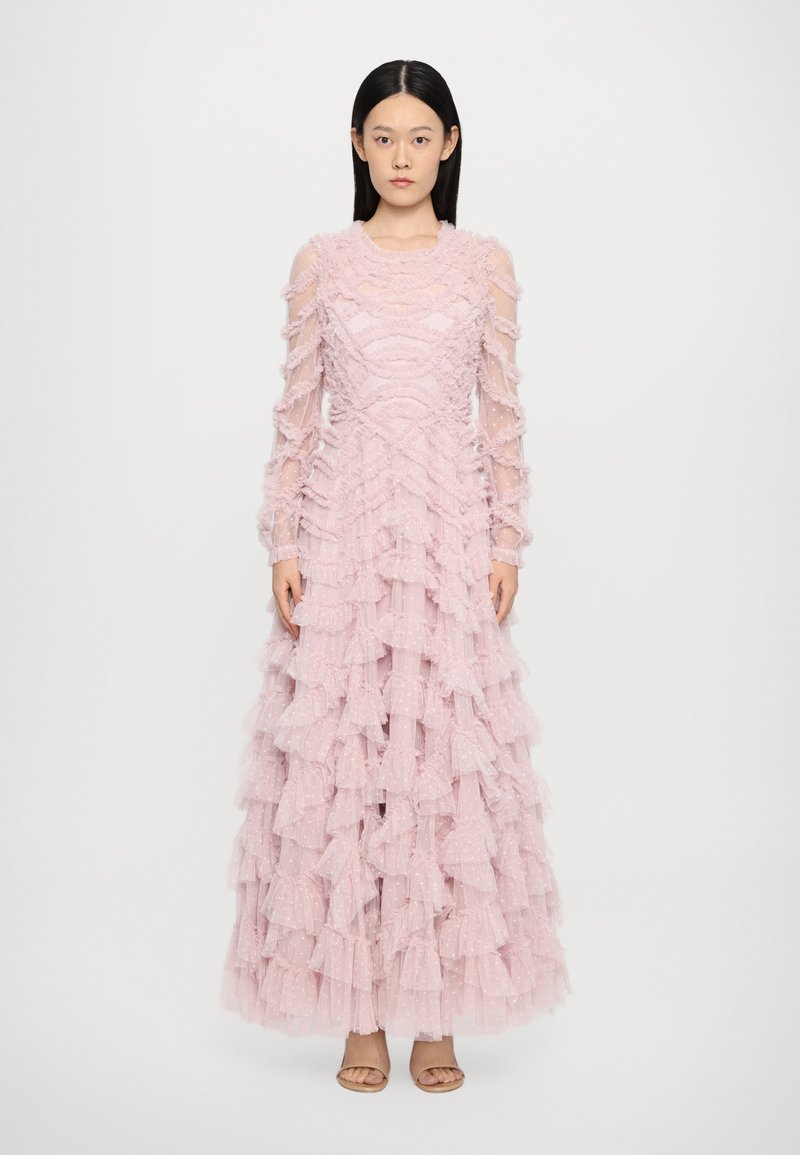 Lange roze jurk met een gelaagd ruffle ontwerp, doorzichtige lange mouwen, gestructureerde stof en een ronde halslijn. Sandalen maken de look compleet.