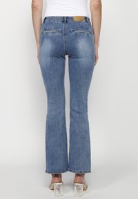 Blå utsvängda jeans med hög midja, tillverkade av denim. Har bakfickor, en brun läderetikett vid midjan och en slät yta.