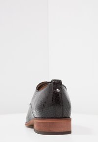 Scarpa in finta pelle nera con un motivo rettiliano testurizzato, tacco in legno marrone e una piccola linguetta sul retro con un rivetto argentato.