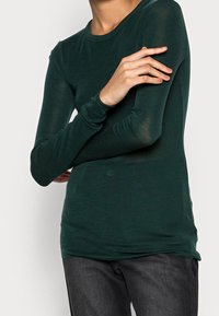 Pitkähihaista tummanvihreää paitaa, joka on valmistettu kevyestä materiaalista. Ominaisuuksiin kuuluu slim fit -leikkaus, pyöreä kaula-aukko ja hienovarainen kuviointi.