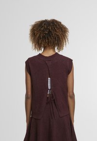 Vest tricotat burgund cu guler rotund, mâneci scurte și o decupare pe spate legată cu un șnur. Textură moale, design casual.