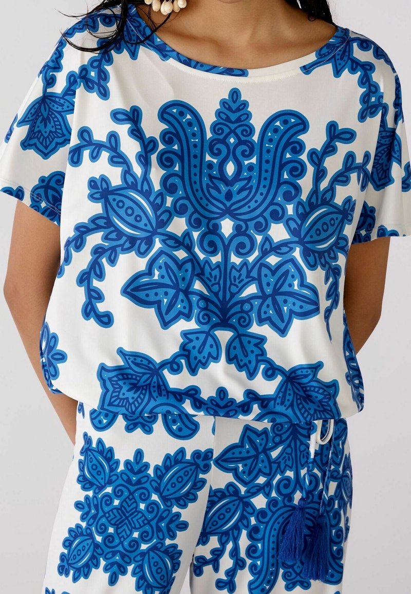 blå og hvid mønstrede kortærmede top med indviklede blomsterdesigns, rund halsudskæring og løs pasform, lavet af letvægtsstof.
