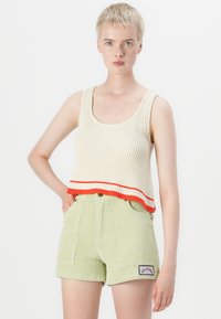 Kremfarget ribbestrikket tanktop med røde striper i kanten, kombinert med grønne cordshorts med frontlommer og et lappemerke.