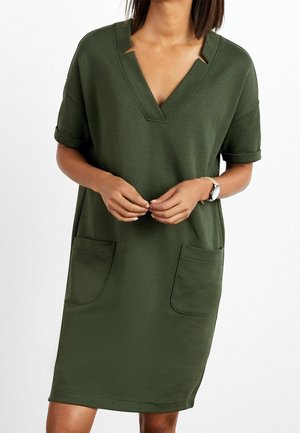 Zielona sukienka do kolan wykonana z miękkiego materiału. Posiada dekolt w serek, podwinięte krótkie rękawy oraz dwie przednie kieszenie. Prosty design bez wzorów.