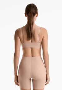 Miękki, nagi, bezszwowy stanik z regulowanymi ramiączkami oraz dopasowane wysokie szorty, wykonane z gładkiego, elastycznego materiału o minimalistycznym wzorze.