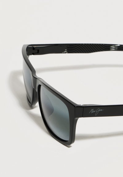 Μαύρα ορθογώνια γυαλιά ηλίου Maui Jim με πολωτικούς γκρι φακούς και διακριτικό λογότυπο στο πλαϊνό μπράτσο, εμφανιζόμενα υπό γωνία σε λευκό φόντο.