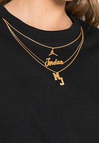 Guldpläterade halsband har en stiliserad "Jordan"-logotyp, en "MJ"-hänge och en Jumpman-emblem, bärs över en svart skjorta.
