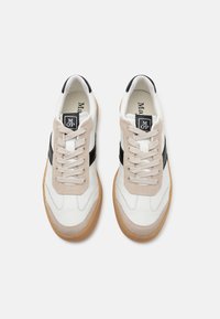 Białe i beżowe sneakersy z czarnymi akcentami, wykonane z mieszanki zamszu i skóry, z zaokrąglonym noskiem, wiązane na przodzie, z gumową podeszwą.