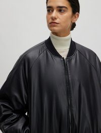 Zwarte leren bomberjack met geribde halslijn. Kenmerken zijn een ritssluiting, een relaxte pasvorm en een gladde textuur.