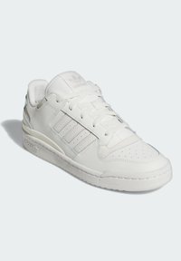Sapatilhas brancas Adidas com parte superior em couro, biqueira perfurada, fecho com atacadores, três riscas de lado e sola acolchoada sobre um fundo claro.