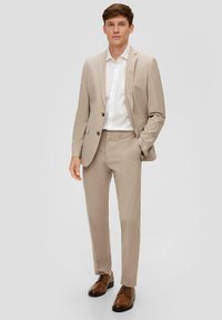 Traje beige con blazer ajustado, pantalones a juego y camisa blanca. Zapatos de vestir marrones completan el conjunto. Tejido suave y ligero.