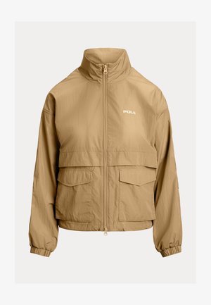 Jachetă ușoară bej, cu guler înalt, închidere cu fermoar frontal, două buzunare pe piept și mansete elastice. Prezintă logo-ul "Polo" în alb.