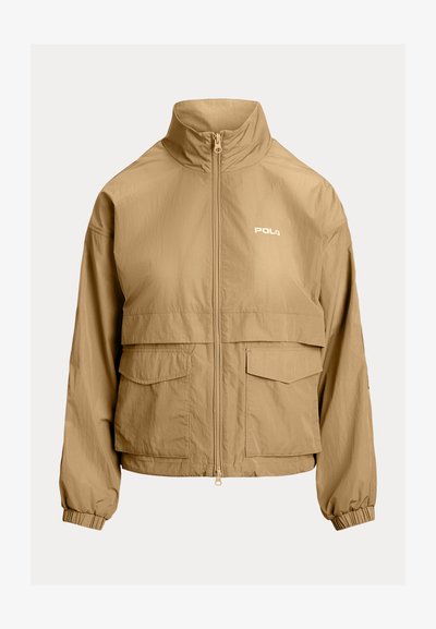 Bežs vieglais jakas ar augstu apkakli, priekšējo rāvējslēdzēju, divām krūšu kabatām un elastīgām aprocēm. Funkcijas "Polo" logo baltā krāsā.