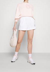 Person wearing light pink Nike sweatshirt, white shorts, white socks, and white Nike sneakers, holding a soft textured beige handbag.