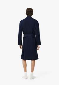 Robe blu navy con maniche lunghe, cintura con cravatta in vita e orlo fino al ginocchio. Tessuto morbido con una texture liscia.