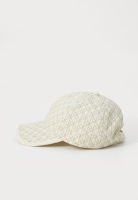 Beige pet met een ruitpatroon in lichtbruin, gemaakt van textuurstof. Beschikt over een gebogen klep en een gestikte bovenknop.