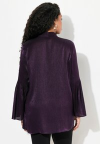 Blusa metallica viola con texture a coste, maniche a campana lunghe e yoke posteriore. Il tessuto morbido drappeggia in modo elegante.