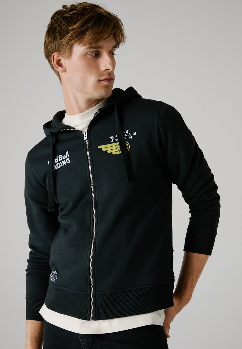 Sudadera con cremallera negra y capucha, que presenta un gráfico amarillo y un logo en el pecho, con puños y dobladillo acanalados, hecha de una suave mezcla de algodón.
