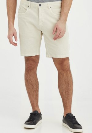 Knelange, lyse shorts laget av teksturert stoff med knappelukking, med frontlommer, sammen med svarte joggesko.