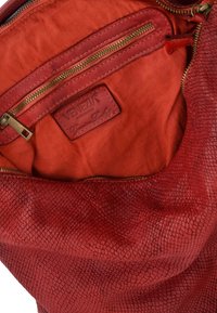 Rød lædertaske med et tekstureret, skællet mønster. Indersiden har en glat rød foring, en lynlåslomme og et mærket lædertag.