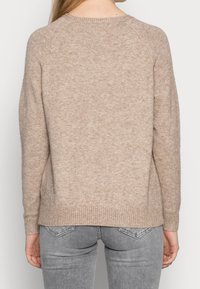 Beige stickad tröja med rundad krage, raglanärmar och ribbad nederkant och ärmslut. Mjuk textur med en något lös passform.